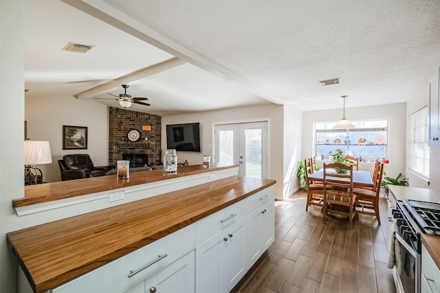 kitchen with white cabinets, decorative light fixtures, a textured ceiling, wooden counters, and gas stove