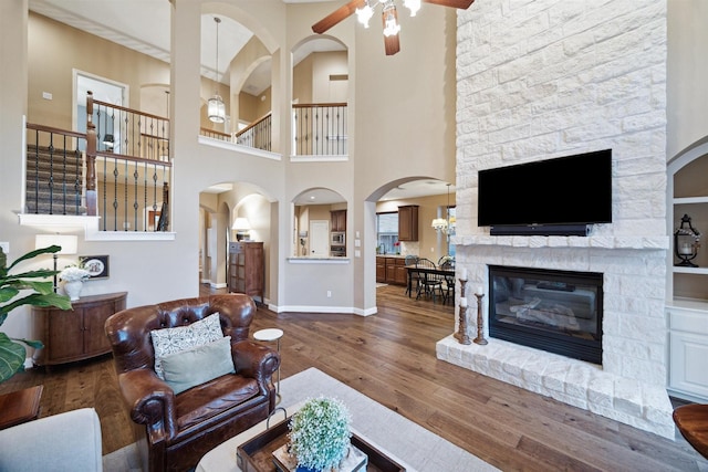 living room featuring a high ceiling, wood-type flooring, ceiling fan, and a stone fireplace