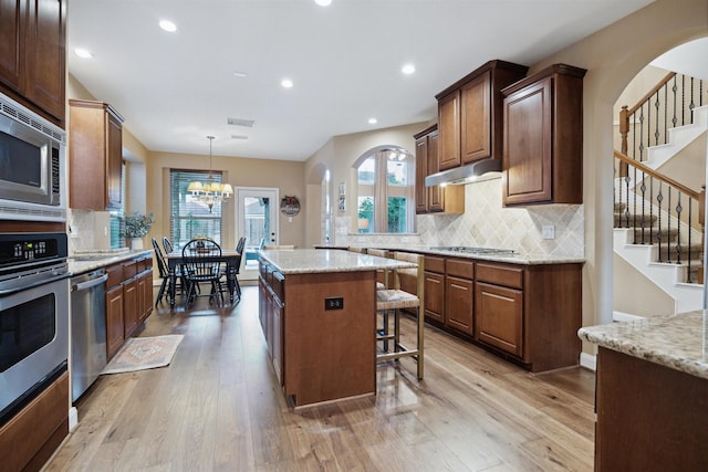 kitchen with stainless steel appliances, a center island, light hardwood / wood-style flooring, backsplash, and light stone countertops