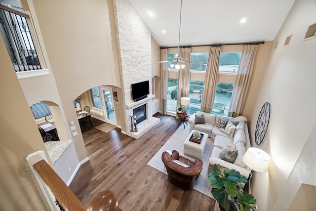 living room with hardwood / wood-style floors, high vaulted ceiling, ceiling fan, and a stone fireplace