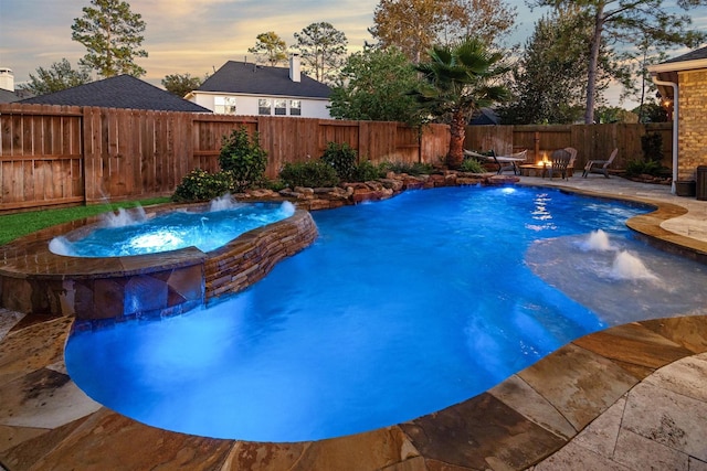 pool at dusk featuring a patio, pool water feature, and an in ground hot tub