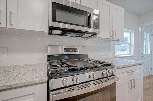 kitchen with appliances with stainless steel finishes, light stone counters, white cabinets, light hardwood / wood-style flooring, and tasteful backsplash