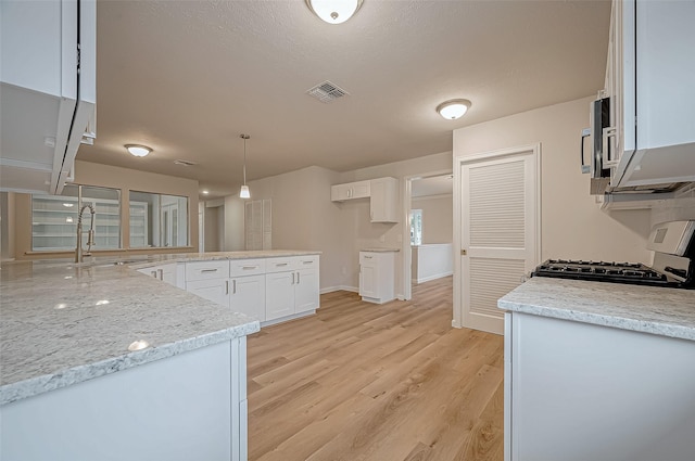 kitchen with sink, white cabinetry, light stone counters, stove, and hanging light fixtures