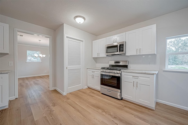 kitchen with white cabinetry, light hardwood / wood-style floors, backsplash, a chandelier, and appliances with stainless steel finishes