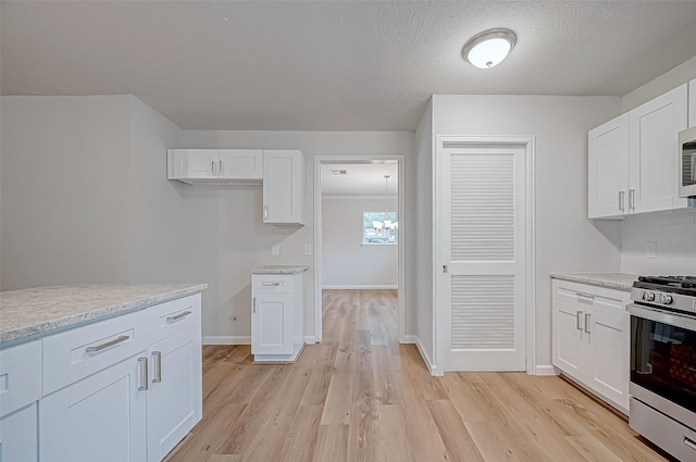 kitchen with stainless steel appliances, white cabinetry, light wood-type flooring, and a notable chandelier