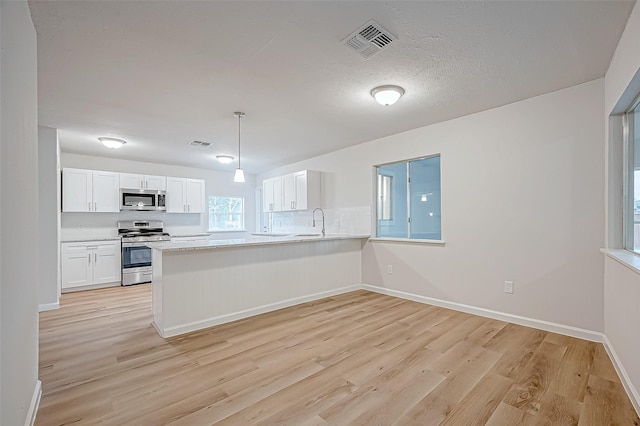 kitchen featuring decorative light fixtures, white cabinets, light hardwood / wood-style floors, kitchen peninsula, and appliances with stainless steel finishes