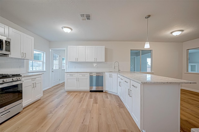 kitchen with stainless steel appliances, kitchen peninsula, pendant lighting, decorative backsplash, and white cabinetry