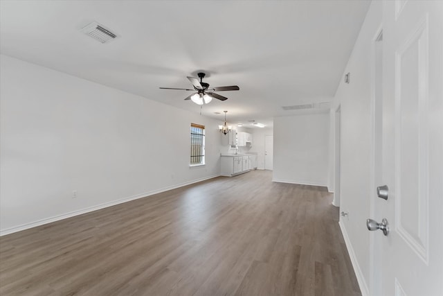 unfurnished living room featuring ceiling fan with notable chandelier and hardwood / wood-style flooring