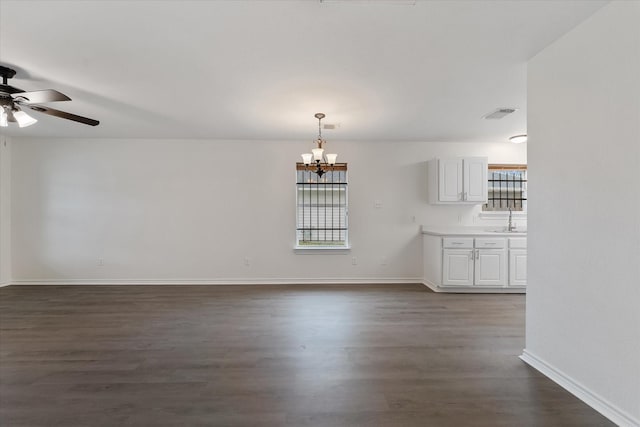 interior space featuring ceiling fan with notable chandelier, a healthy amount of sunlight, and dark wood-type flooring