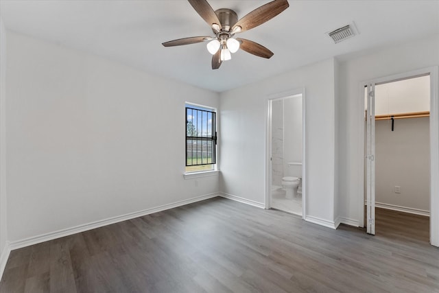 unfurnished bedroom featuring connected bathroom, dark wood-type flooring, ceiling fan, and a spacious closet