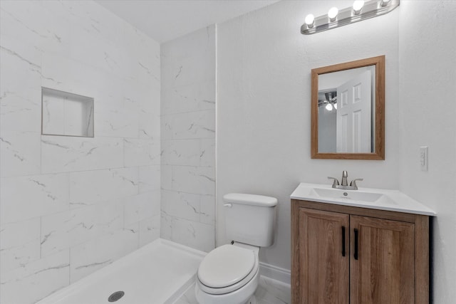 bathroom featuring toilet, tiled shower, and vanity