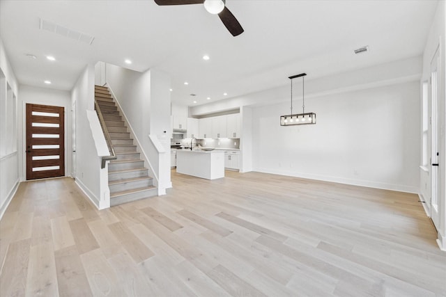 unfurnished living room with sink, ceiling fan, and light wood-type flooring