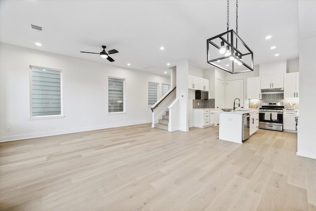 kitchen with appliances with stainless steel finishes, an island with sink, ceiling fan, pendant lighting, and white cabinets