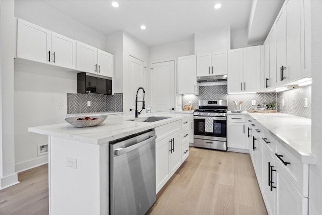 kitchen with a center island with sink, stainless steel appliances, light wood-type flooring, sink, and white cabinetry