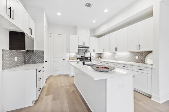 kitchen featuring white cabinets, a center island with sink, light wood-type flooring, and decorative backsplash