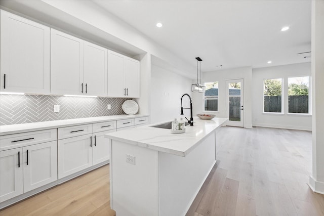 kitchen with sink, a center island with sink, white cabinets, and pendant lighting