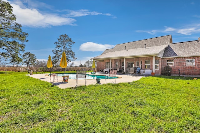 back of house with brick siding, fence, a lawn, a fenced in pool, and a patio area