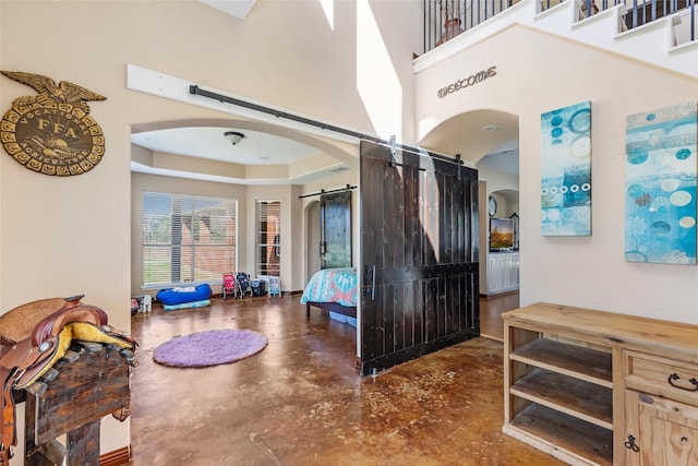 interior space with arched walkways, a raised ceiling, a high ceiling, a barn door, and finished concrete floors