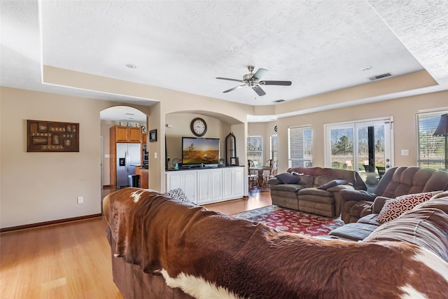 living room featuring a textured ceiling, arched walkways, visible vents, baseboards, and light wood-type flooring