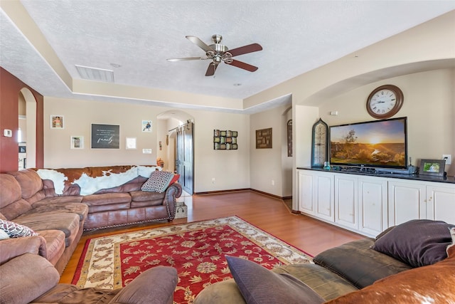 living area featuring light wood finished floors, visible vents, arched walkways, and a textured ceiling