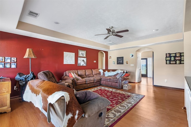 living area featuring arched walkways, visible vents, a ceiling fan, wood finished floors, and baseboards