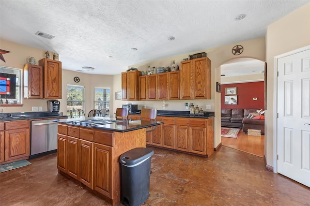 kitchen with a kitchen island, visible vents, appliances with stainless steel finishes, brown cabinetry, and dark countertops