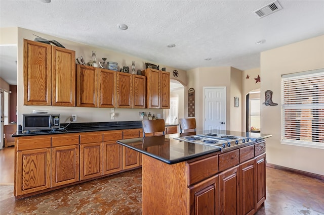 kitchen with stainless steel appliances, a center island, brown cabinets, and dark countertops