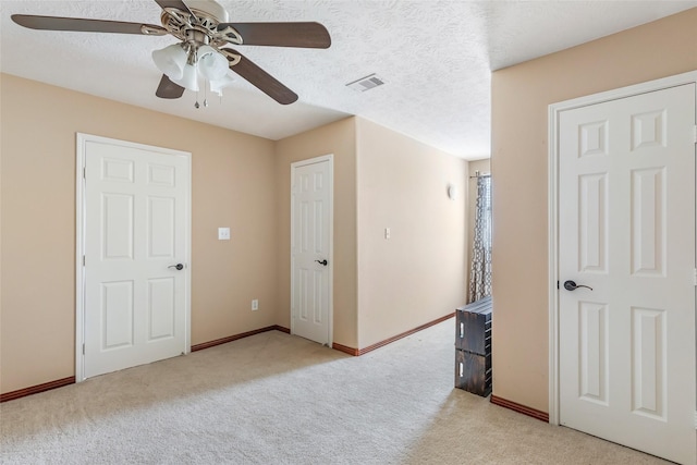 unfurnished bedroom featuring visible vents, light colored carpet, a textured ceiling, and baseboards