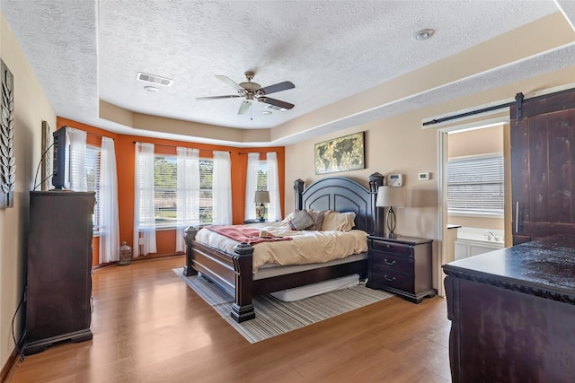 bedroom with a barn door, visible vents, a raised ceiling, light wood-style flooring, and a textured ceiling