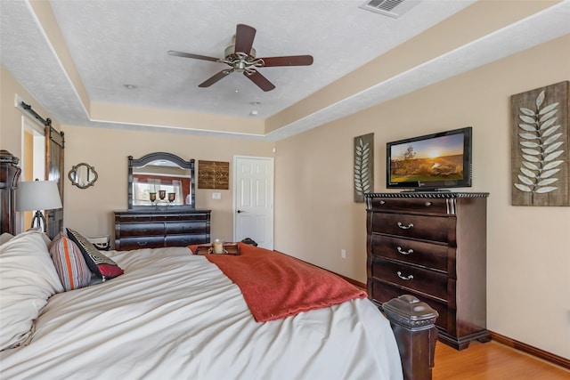 bedroom with light wood finished floors, a barn door, baseboards, a tray ceiling, and a textured ceiling