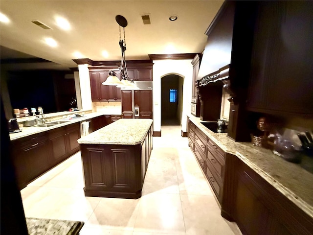 kitchen featuring paneled built in refrigerator, a center island, light stone countertops, sink, and decorative light fixtures