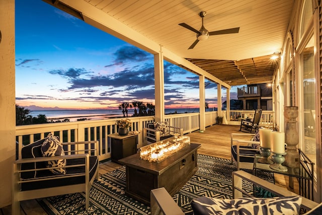 deck at dusk with an outdoor fire pit, ceiling fan, and a water view