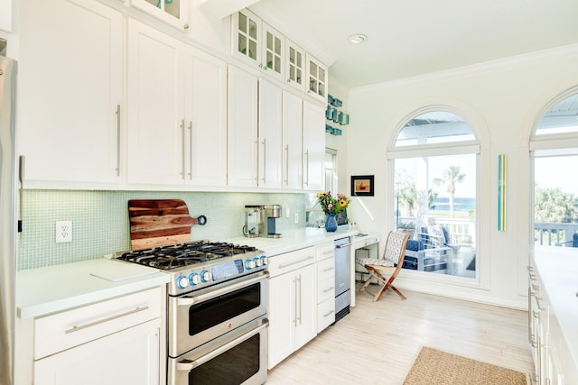 kitchen with a healthy amount of sunlight, stainless steel appliances, backsplash, crown molding, and white cabinets