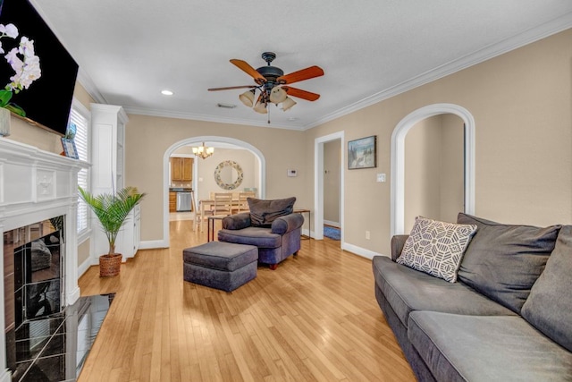 living room with a tiled fireplace, ornamental molding, ceiling fan with notable chandelier, and wood-type flooring