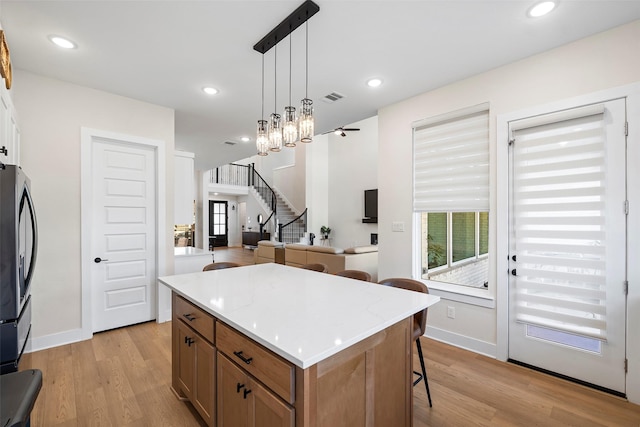 kitchen featuring light wood-type flooring, hanging light fixtures, stainless steel refrigerator, a chandelier, and a center island