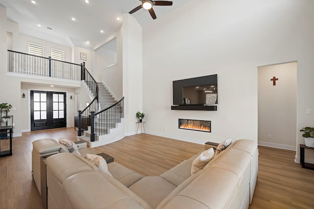 living room featuring ceiling fan, a high ceiling, hardwood / wood-style floors, and french doors