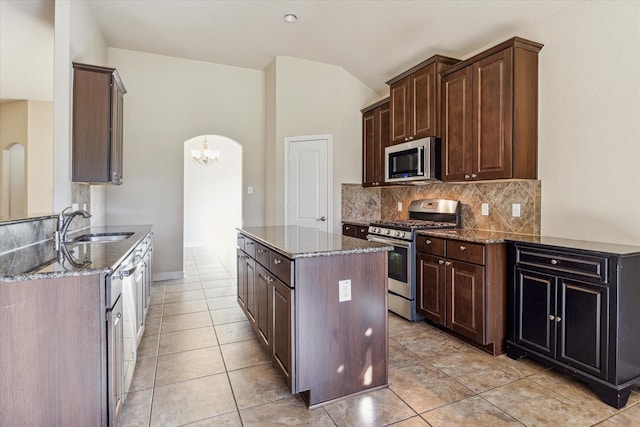 kitchen featuring sink, light tile patterned flooring, dark stone countertops, backsplash, and appliances with stainless steel finishes