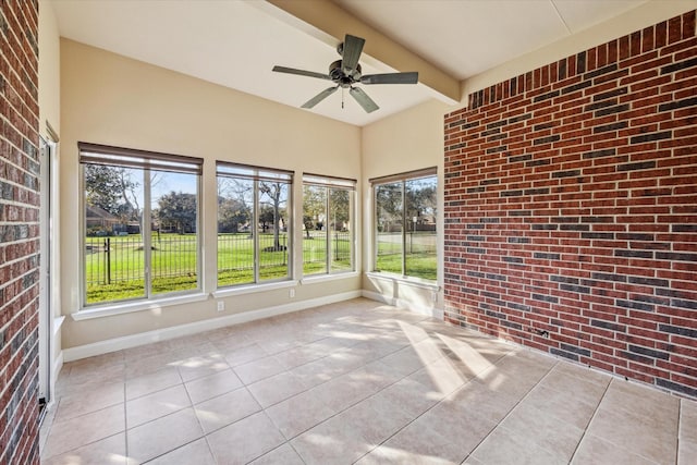 unfurnished sunroom featuring ceiling fan, a healthy amount of sunlight, and beam ceiling