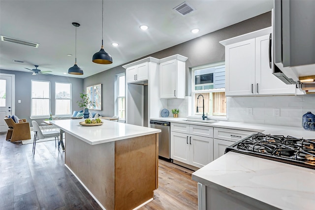 kitchen featuring sink, white cabinetry, stainless steel appliances, light stone countertops, and decorative light fixtures