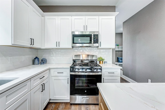 kitchen with appliances with stainless steel finishes, white cabinets, backsplash, light stone counters, and dark wood-type flooring