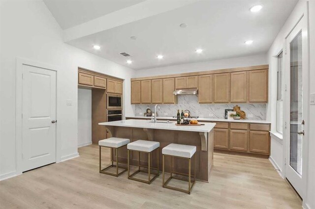 kitchen with sink, black microwave, a kitchen breakfast bar, light hardwood / wood-style flooring, and a kitchen island with sink