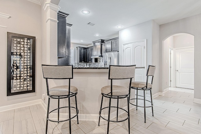 kitchen with decorative backsplash, a breakfast bar, kitchen peninsula, and stainless steel fridge