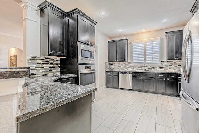 kitchen with stainless steel appliances, light tile patterned floors, dark stone countertops, and backsplash