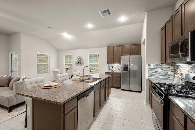 kitchen featuring appliances with stainless steel finishes, sink, vaulted ceiling, light stone counters, and a center island with sink