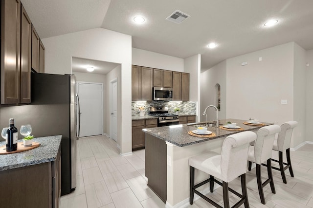 kitchen featuring lofted ceiling, stainless steel appliances, dark stone counters, sink, and a center island with sink