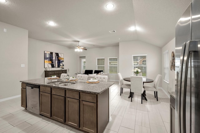 kitchen featuring a center island with sink, stainless steel appliances, stone countertops, a textured ceiling, and sink