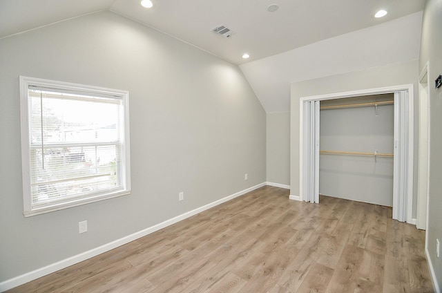 unfurnished bedroom with multiple windows, light wood-type flooring, a closet, and vaulted ceiling