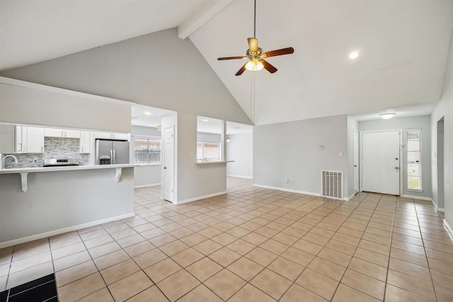 unfurnished living room featuring beamed ceiling, ceiling fan, light tile patterned floors, a wealth of natural light, and high vaulted ceiling