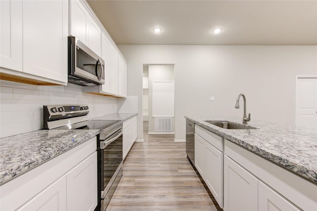 kitchen with appliances with stainless steel finishes, light wood-type flooring, light stone counters, sink, and white cabinetry