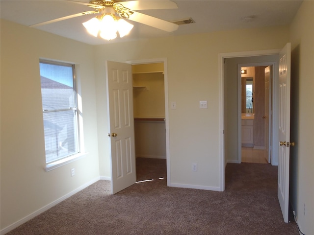 unfurnished bedroom with dark carpet, ceiling fan, multiple windows, and a spacious closet